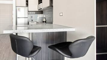 Una cocina moderna con barra, dos taburetes negros y un refrigerador de acero inoxidable.