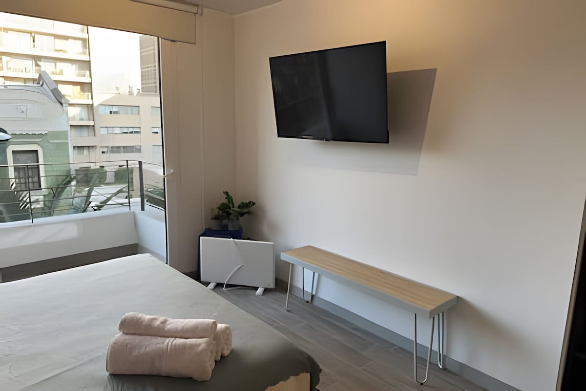Une chambre d’hôtel moderne, équipée d’un lit, d’un téléviseur fixé au mur, d’une petite table et d’une plante en pot.