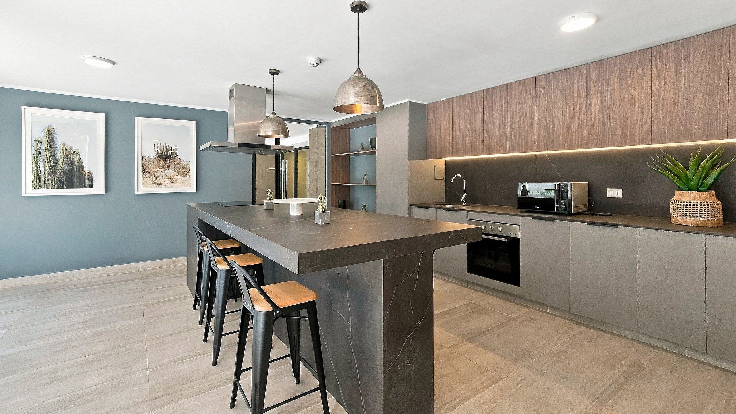 Una cocina moderna con una isla central, taburetes de bar, iluminación colgante y electrodomésticos integrados.