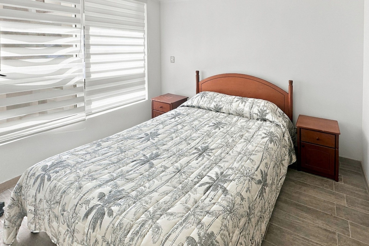Une chambre à coucher avec un lit, des tables de chevet, une fenêtre avec des stores et un plancher en bois.