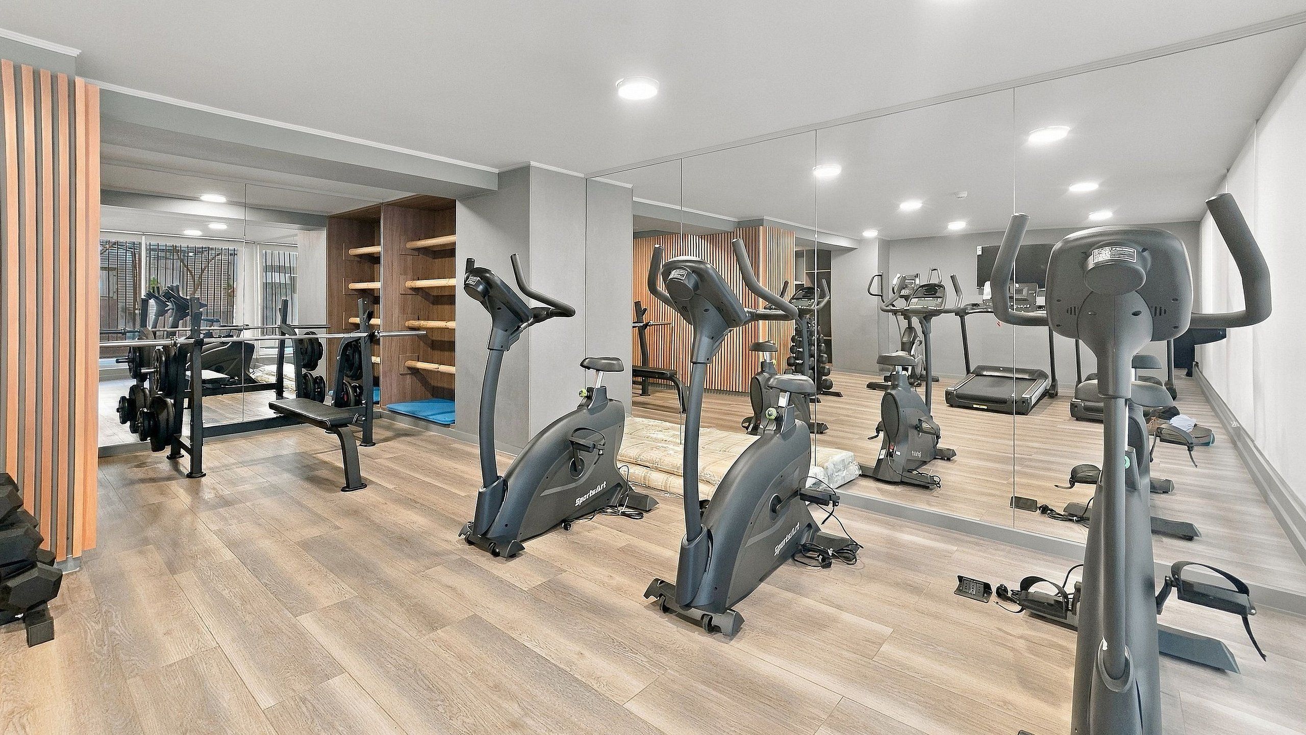 Un gimnasio con diversas máquinas de cardio, equipo de levantamiento de pesas y espejos en las paredes.