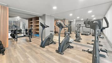 Un gimnasio con diversas máquinas de cardio, equipo de levantamiento de pesas y espejos en las paredes.