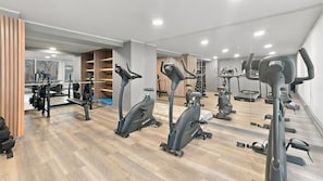 Un gimnasio con diversas máquinas de cardio, equipo de levantamiento de pesas y espejos en las paredes.