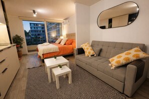 A modern bedroom with a bed, a sofa, a small table, and a mirror.