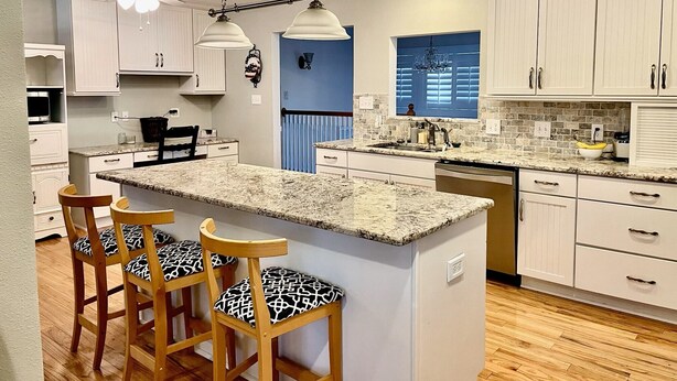 A kitchen with a central island, wooden chairs, white cabinets, and a blue accent wall. - Spacious 4-bed house in the woods of beautiful Monument by the Air Force Academy (Monument)