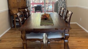 A dining room with a wooden table, chairs, a chandelier, and a view through a glass door to an outdoor area with a red fence and chairs. - Spacious 4-bed house in the woods of beautiful Monument by the Air Force Academy (Monument)