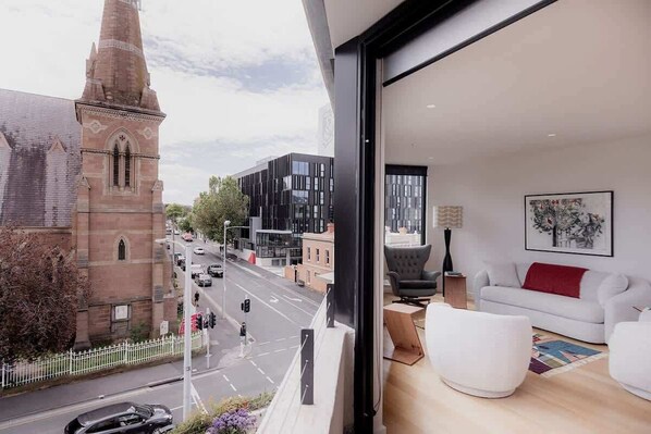 A modern living room with a large window overlooking a street and a church. - The Rox - Inner City Luxury (Hobart)