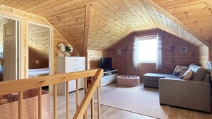 Acogedor dormitorio en ático con vigas de madera, sofá, televisor y ventana.