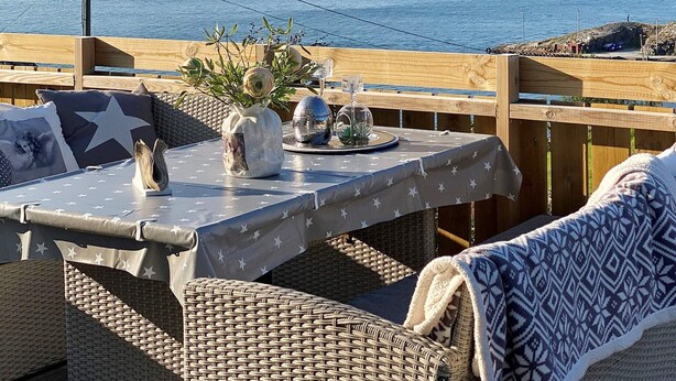 Una terraza de madera con una mesa lista para dos, con vista a un cuerpo de agua y colinas.