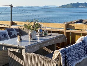 A wooden deck with a table set for two, overlooking a body of water and hills. - 8 Person Holiday Home in Tau (Strand)