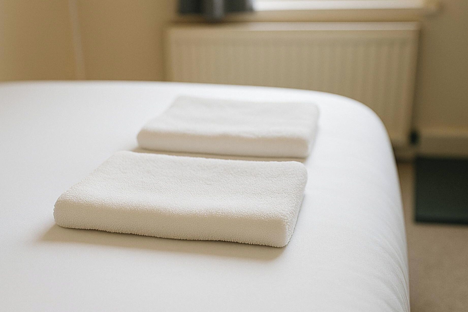 Ein ordentlich bezogenes Bett mit zwei gefalteten weißen Handtüchern darauf.