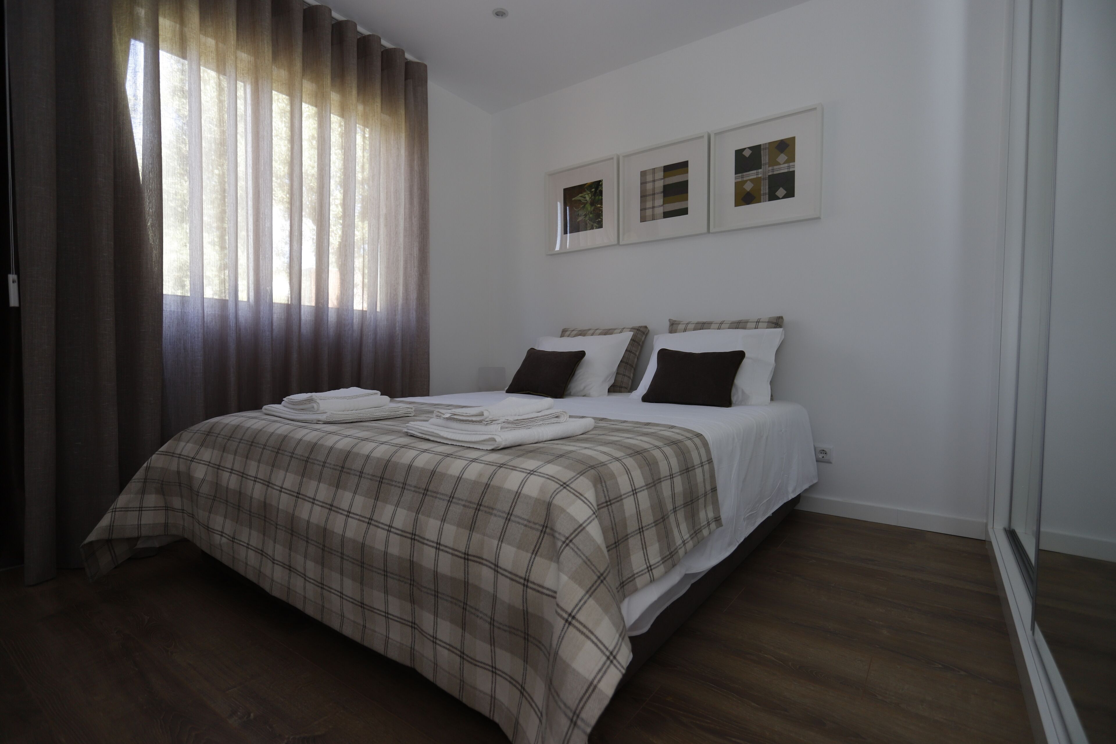 A bedroom with a bed, curtains, and three framed pictures on the wall.