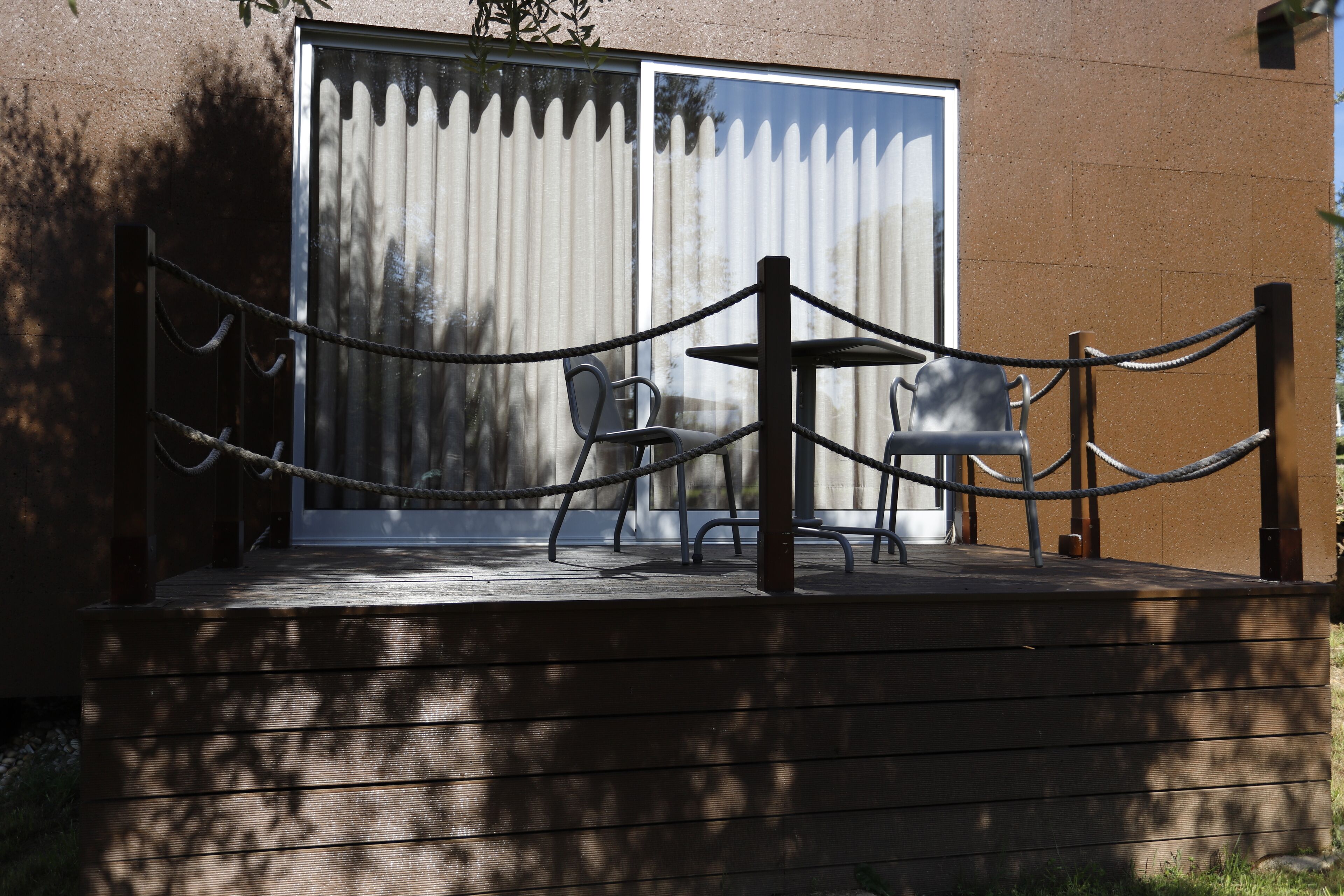 An outdoor seating area with a table and chairs, a rope barrier, and a building with a large window and a door.
