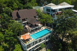 A large house with a swimming pool, multiple balconies, and lush greenery surrounding it.