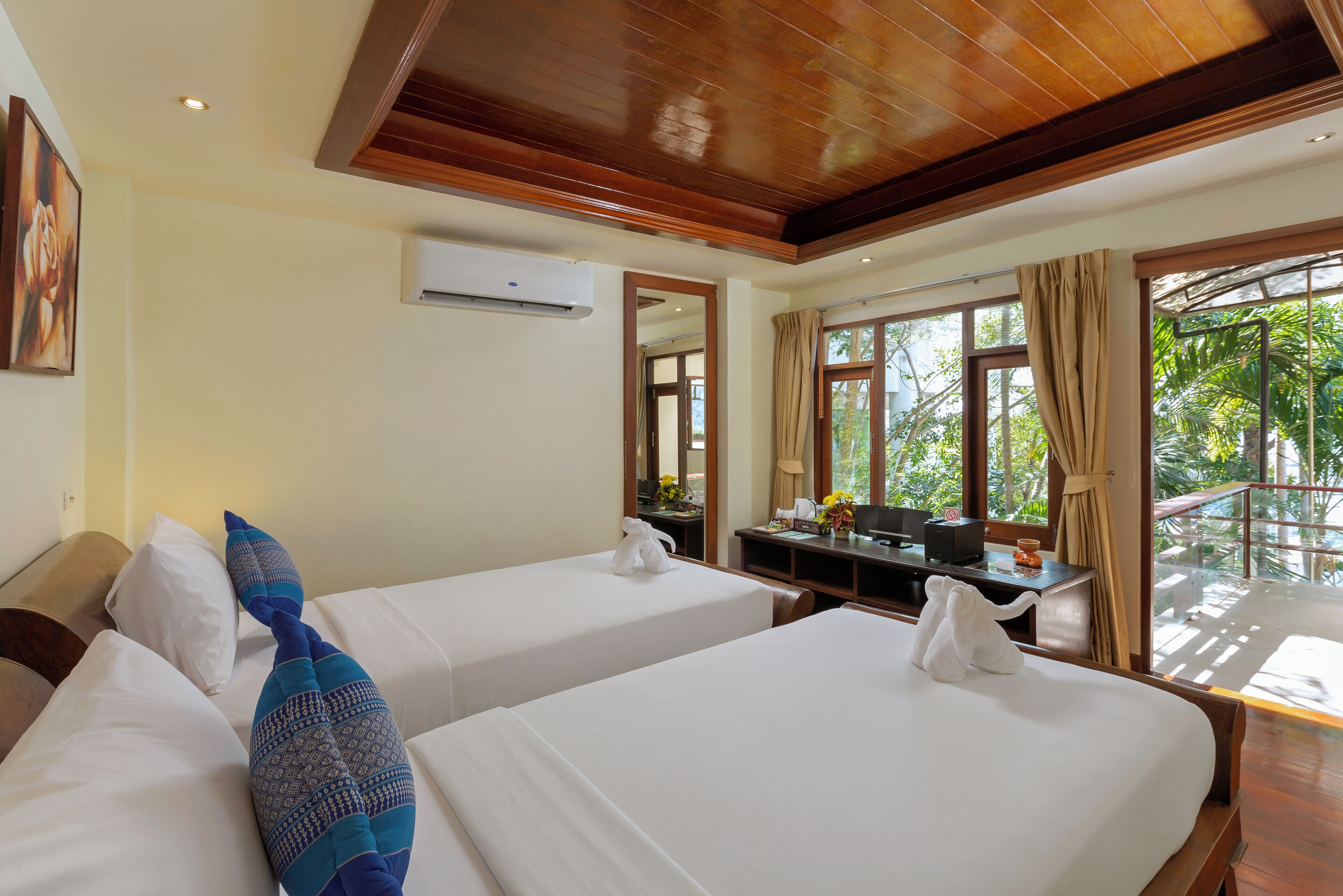A hotel room with two beds, a desk, and a view of greenery.