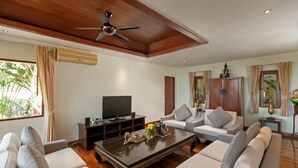 Ein Wohnzimmer mit Deckenventilator, Fernseher, Couchtisch aus Holz und zwei Sofas.