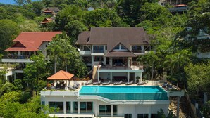 Ein mehrstöckiges Haus mit Swimmingpool, umgeben von üppigem Grün und weiteren Häusern.