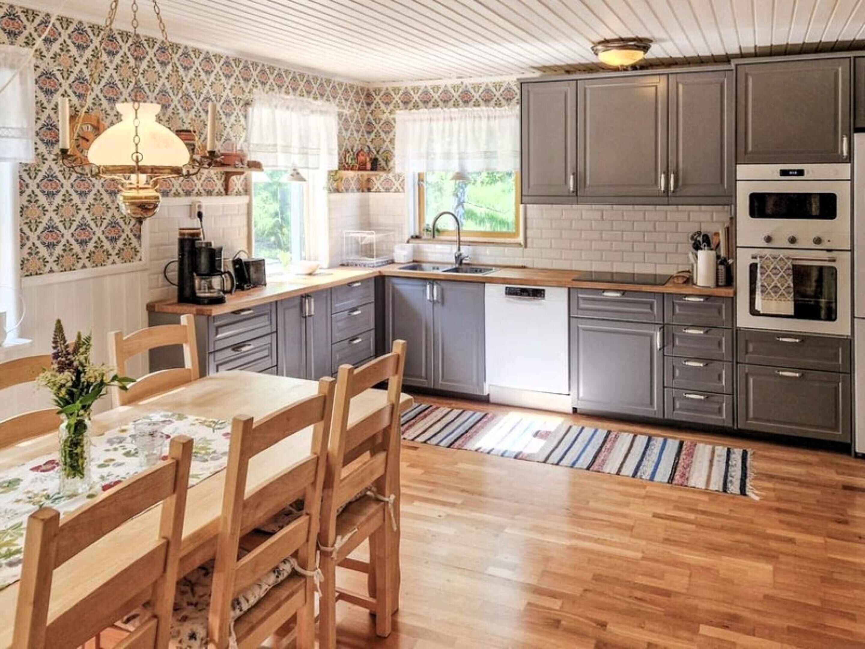 A kitchen with grey cabinets, a wooden dining table, and a hanging light fixture.