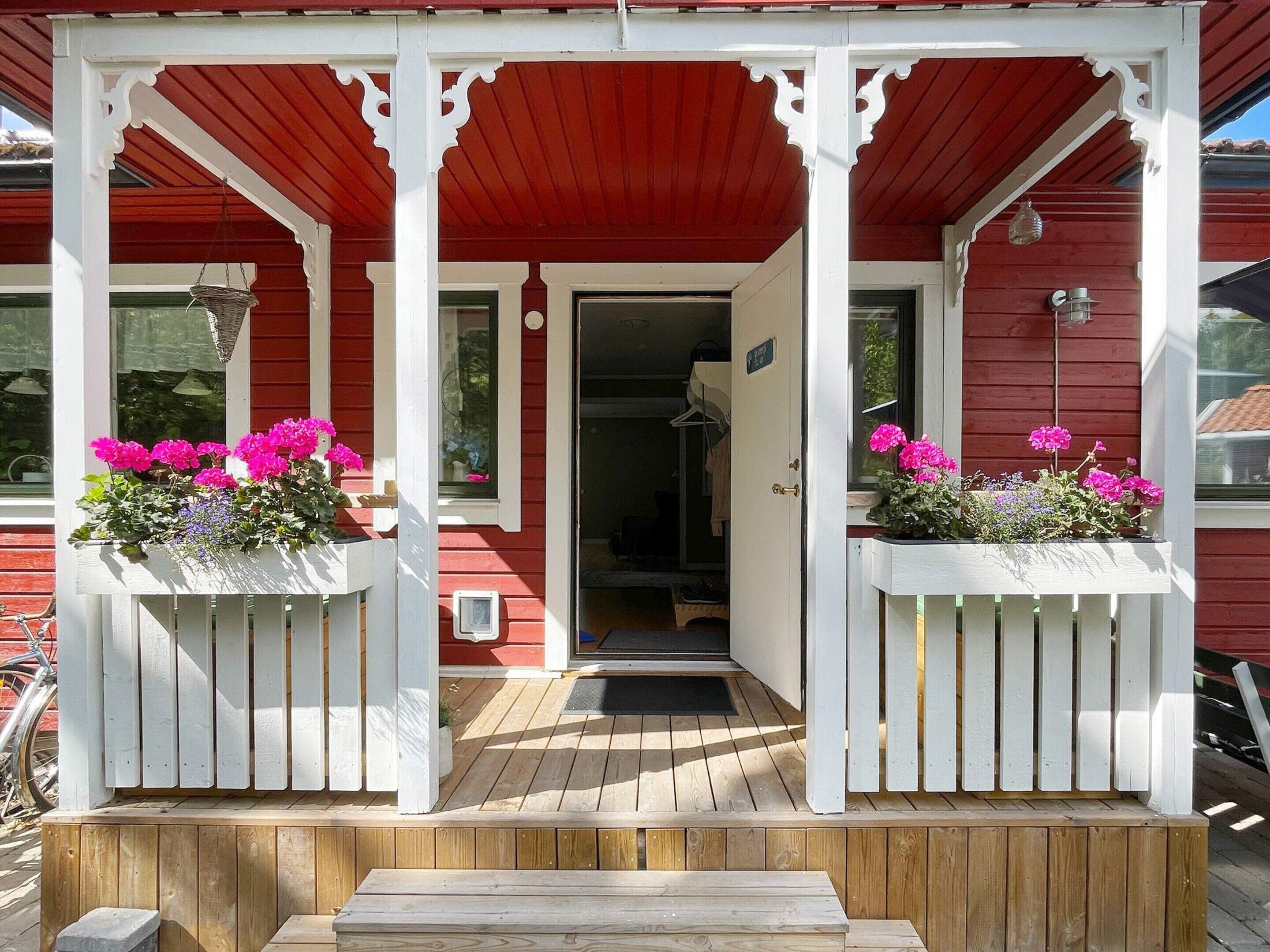 A wooden porch with a red roof and white columns, leading to a door with a small window.