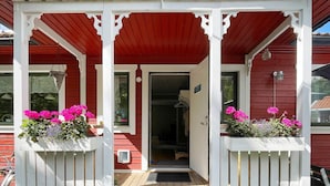 Eine hölzerne Veranda mit rotem Dach und weißen Säulen, die zu einer Tür mit kleinem Fenster führt.