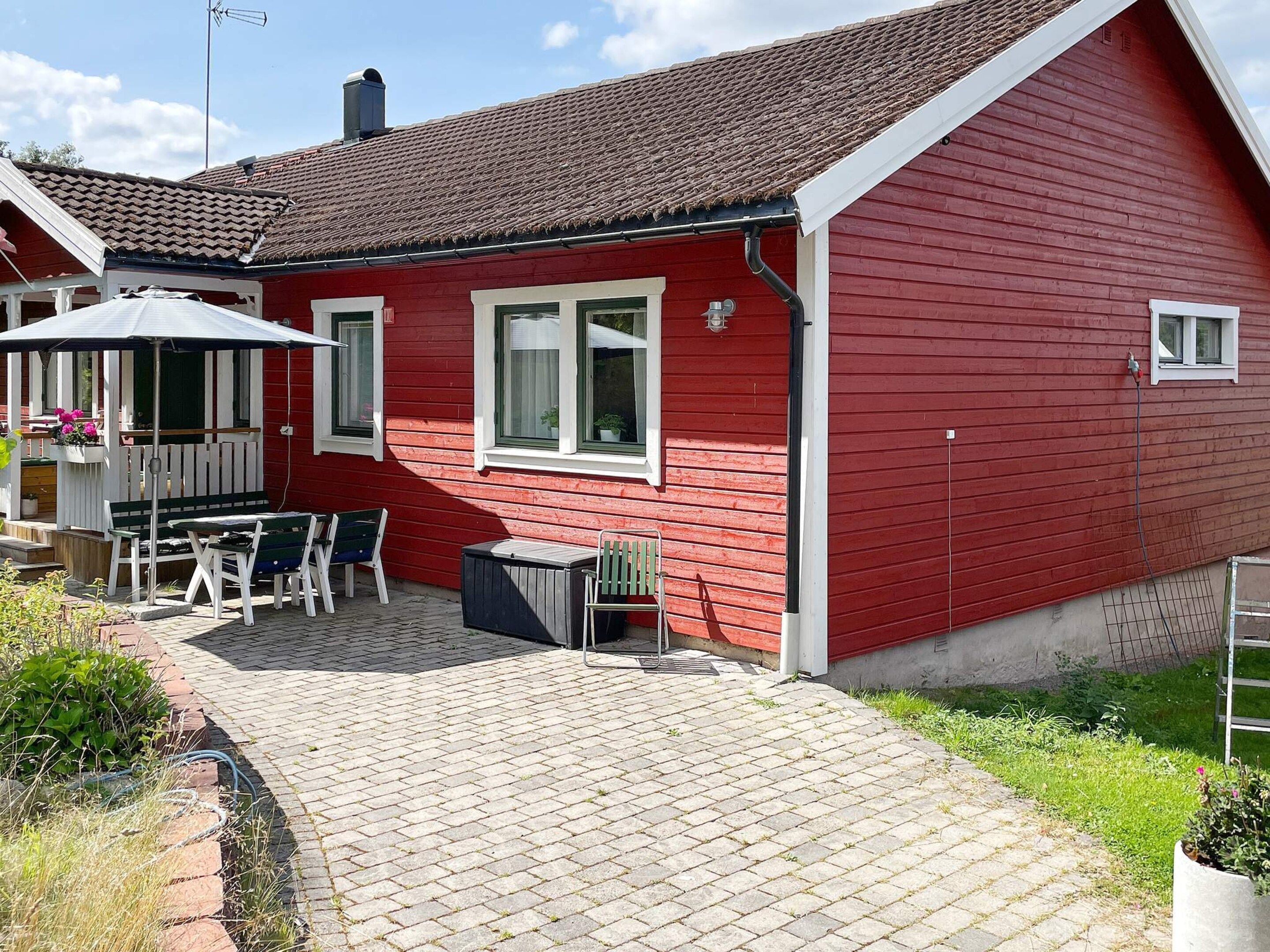 A red house with a tiled roof, a patio with a table and chairs, and a small garden area.