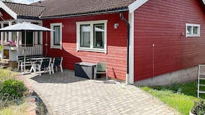 Ein rotes Haus mit Ziegeldach, einer Terrasse mit Tisch und Stühlen sowie ein kleiner Garten.