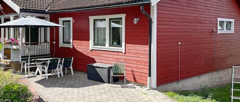 A red house with a tiled roof, a patio with a table and chairs, and a small garden area.
