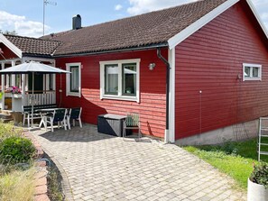 Una casa roja con techo de tejas, un patio con mesa y sillas, y un pequeño jardín.