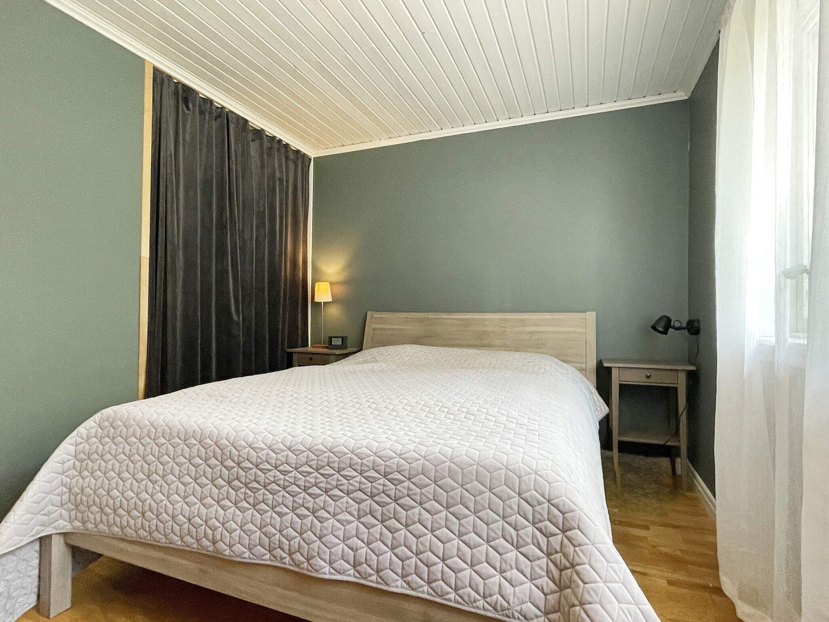 Een hotelkamer met een bed, nachtkastje, lamp en een raam met gordijnen.