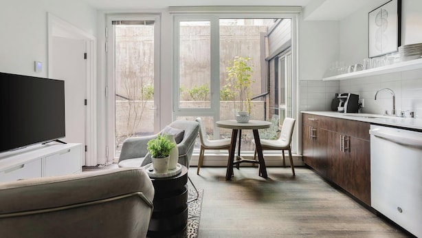 A modern kitchen with a dining area, large windows, and a TV.