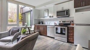A modern kitchen with white cabinets, stainless steel appliances, and a dining area with a grey sofa and table.