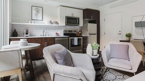 A modern kitchen with white cabinets, a microwave, a refrigerator, and a dining area with two chairs and a table.