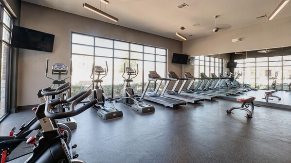 Une salle de sport équipée de tapis de course, de vélos elliptiques et de vélos d’appartement, disposés en rangées.