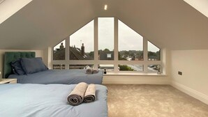 Ein Schlafzimmer mit einem großen Oberlicht, einem Bett mit blauer Bettwäsche und Blick auf Häuser durch die Fenster.