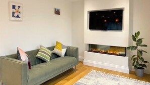 Ein modernes Wohnzimmer mit einem grünen Sofa, einem flachbildfernseher über einem Kamin und einer Topfpflanze.