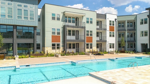 A modern apartment complex with a swimming pool, multiple balconies, and a mix of exterior finishes.