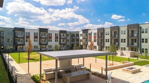 A modern apartment complex with multiple balconies, a covered outdoor seating area, and a well-maintained lawn.