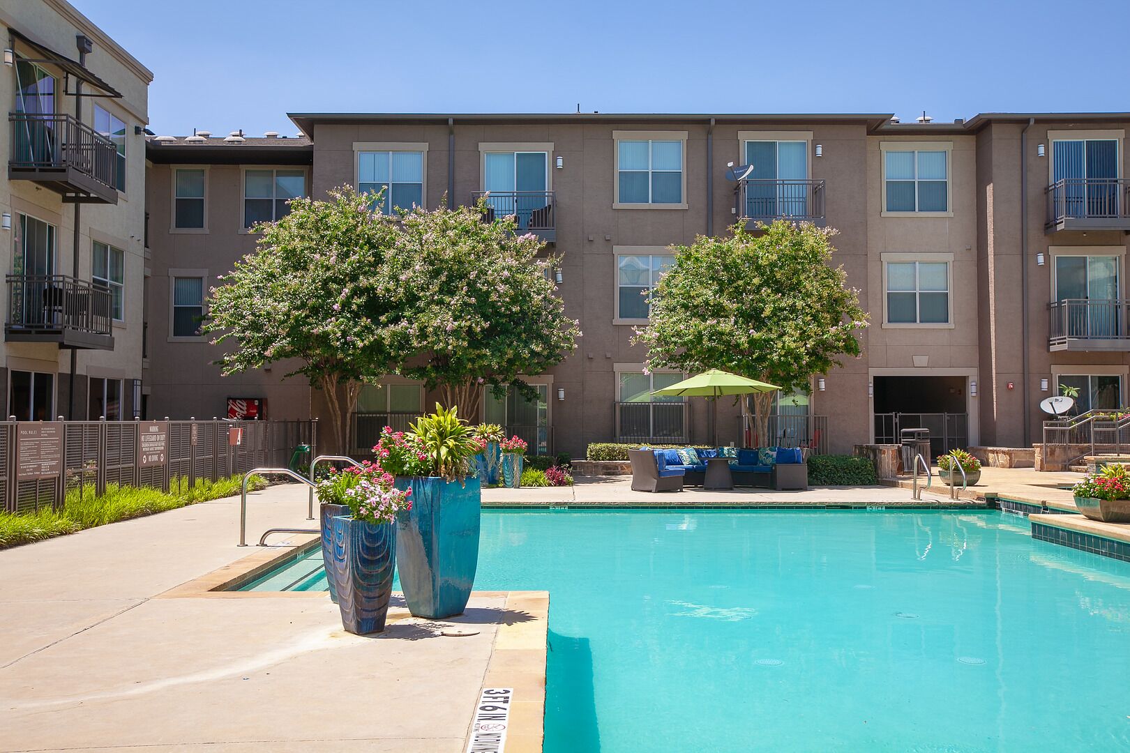 A swimming pool with lounge chairs and potted plants, surrounded by a multi-story building with balconies.
