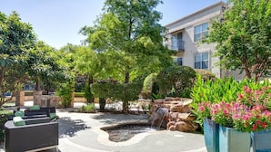 A courtyard with a small waterfall, outdoor seating, and potted plants. - Landing | Stylish Studio, Pool, Gym (Dallas)