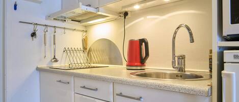 A modern kitchen with a stainless steel sink, a red kettle, and a kettle hook.