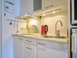 A modern kitchen with a stainless steel sink, a red kettle, and a kettle hook. - 2 Person Holiday Home in Nexo (Nexø)