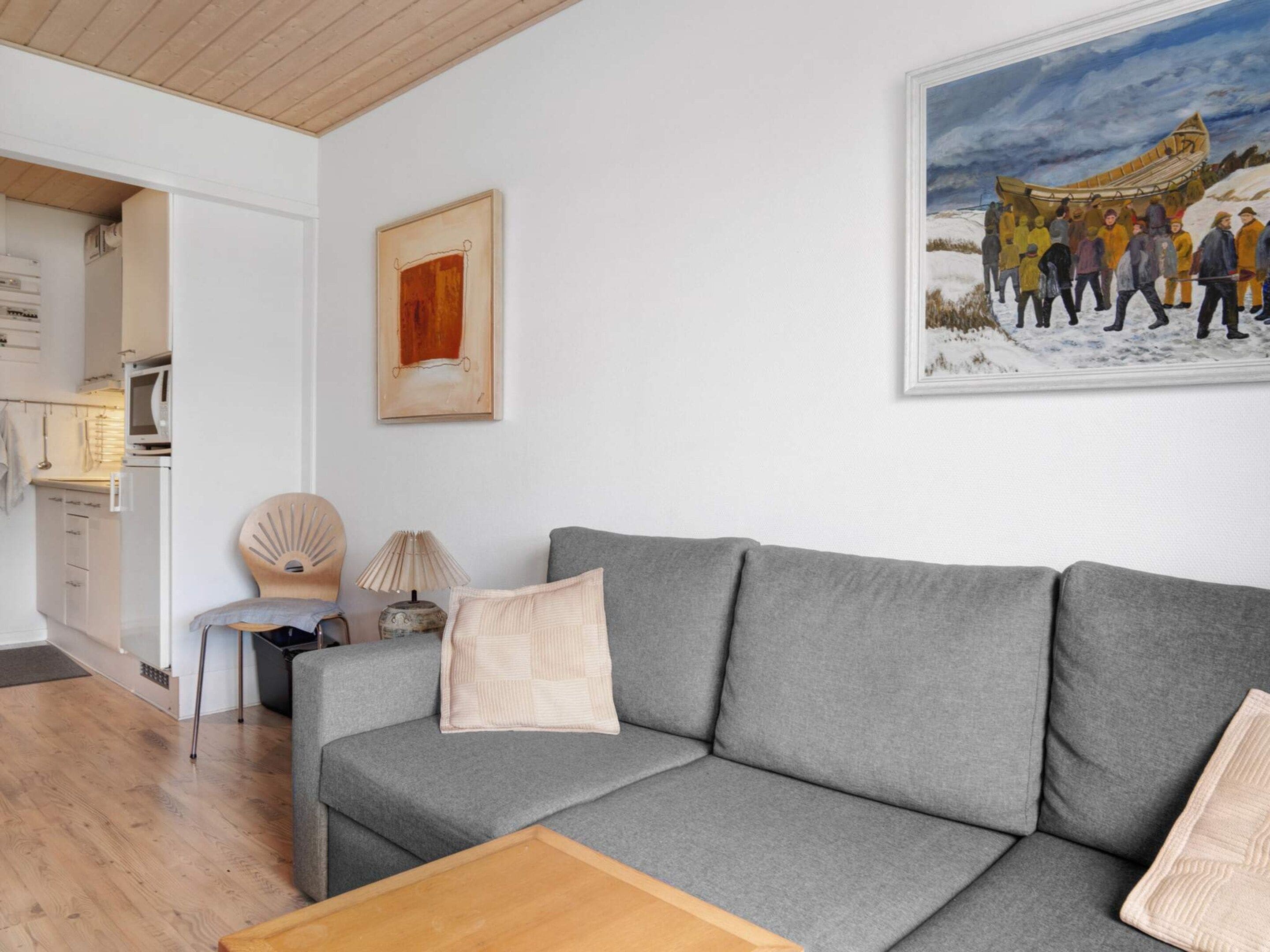 Una sala de estar moderna con un sofá gris, una mesa de centro de madera y un cuadro de un grupo en una canoa en un paisaje nevado.