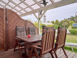 Um deck de madeira com mesa e cadeiras, um portão de madeira e uma pérgula com decoração de pássaro e coruja.
