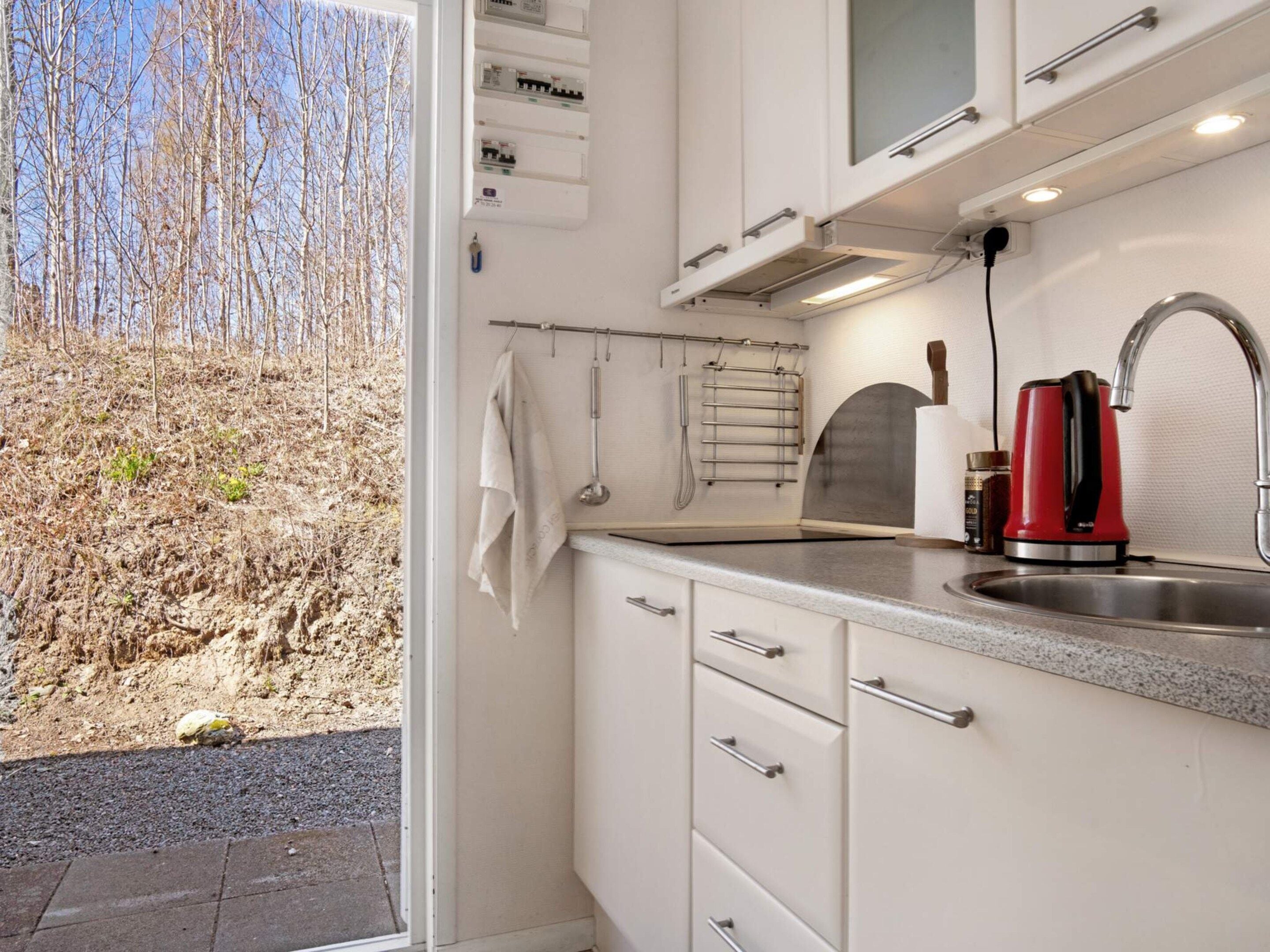 A modern kitchen with a stainless steel sink, a red kettle, and a view of a dry landscape outside.