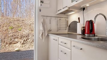 A modern kitchen with a stainless steel sink, a red kettle, and a view of a dry landscape outside.