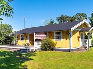 A yellow building with a porch, a flag, and a small garden area.