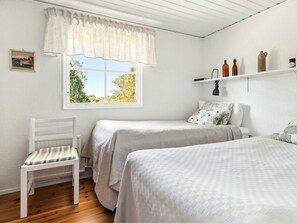 A bedroom with two beds, a chair, a window with a view of trees, and a shelf with bottles and a lamp. - 4 Person Holiday Home in Lottorp (Löttorp)