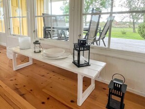 A white bench with a white plate and two black lanterns on it, positioned in front of a window with a view of outdoor furniture. - 4 Person Holiday Home in Lottorp (Löttorp)