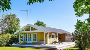 Ein eingeschossiges Gebäude mit Satteldach, einer Veranda mit Sitzbank und einer kleinen Terrassenfläche.
