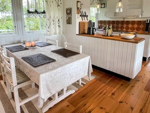 A dining area with a table set for four, a kitchen with a wooden countertop, and a window with curtains. - 4 Person Holiday Home in Lottorp (Löttorp)
